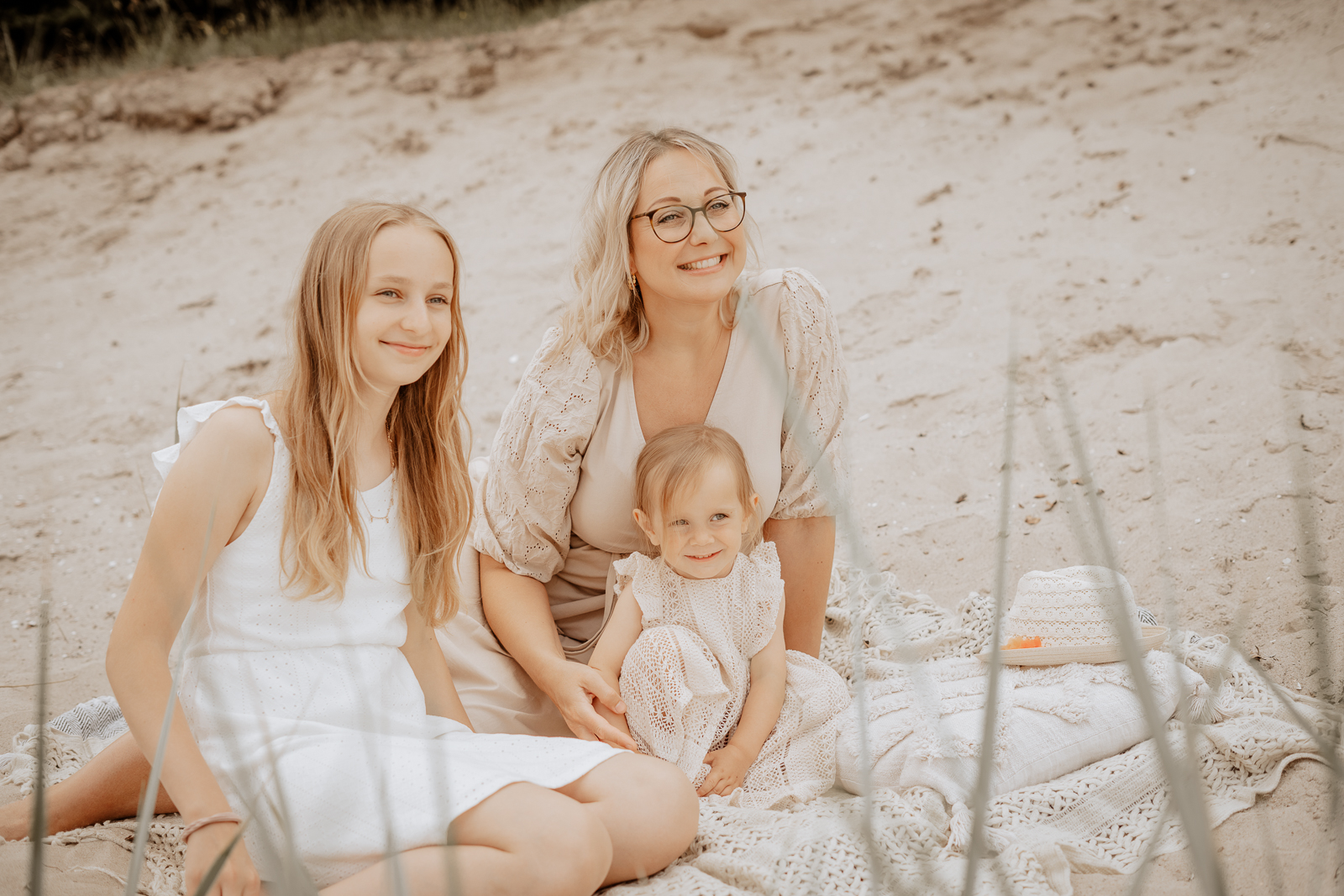 Eine Mutter sitzt mit ihren zwei Töchtern bei einem Mommy & Me-Shooting am Strand und alle lächeln während sie auf die Ostsee schauen. Das Foto erscheint auf der Unterseite zum Ablauf eines Fotoshootings bei dem Punkt zur ersten Kontaktaufnahme.