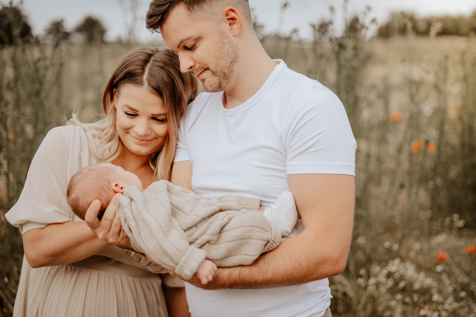 Frisch gebackene Eltern haben ein Outdoor-Newbornshooting. Der Sohn ist erst 14 Tage alt. Beide Eltern schauen verliebt auf ihr kleines Wunder. Das Foto wird auf der Unterseite zum Ablauf eines Fotoshootings zu dem Punkt der Vorbereitung angezeigt.